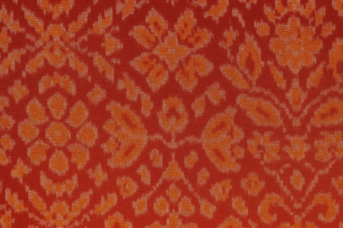 A detailed close-up of authentic Patola fabric showcasing fine double ikat weaving in red and gold with geometric floral motifs.